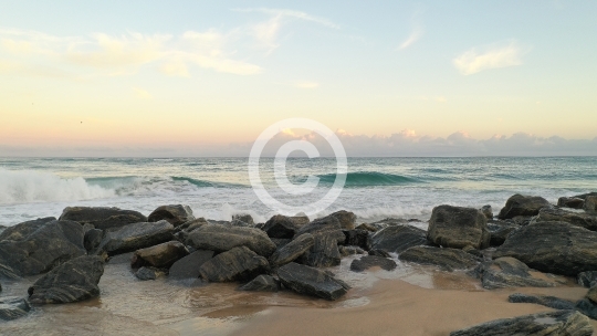 Waves Crashing Over Rocks on Sandy Beach